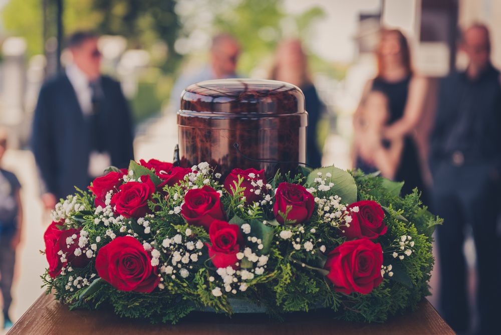 Urna funerária cercada por um arranjo de rosas vermelhas, usada em uma homenagem de despedida, ilustrando o contexto em que muitas pessoas procuram saber quanto custa uma coroa de flores.