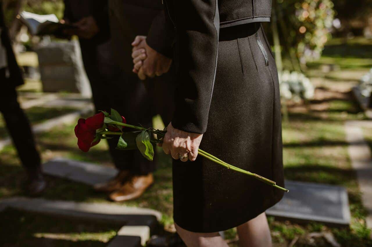 Mulher vestida de preto segurando uma rosa vermelha durante um funeral no cemitério.