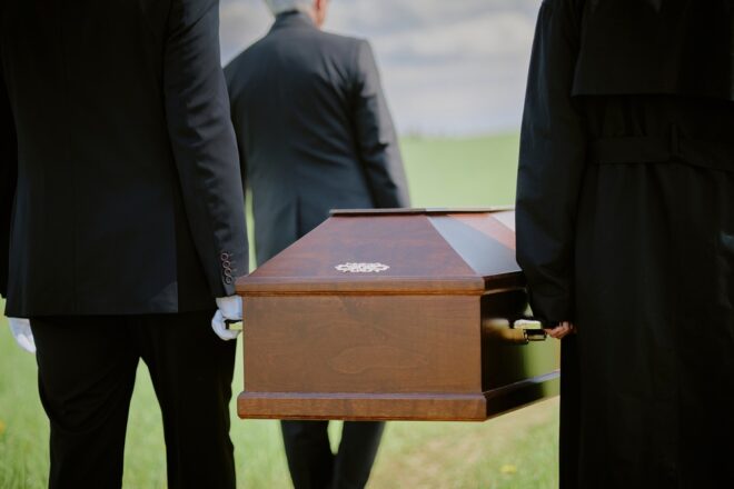 Cortejo fúnebre com caixão sendo conduzido por pessoas vestidas de preto.