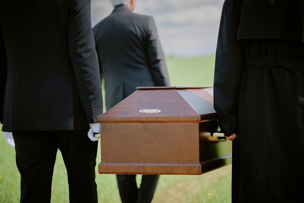 Cortejo fúnebre com caixão sendo conduzido por pessoas vestidas de preto.
