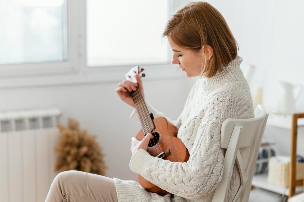 Mulher tocando ukulele com foco na expressão tranquila, em um ambiente iluminado. A imagem transmite uma sensação de serenidade, que pode ser associada ao momento de reflexão e escuta de músicas de luto.